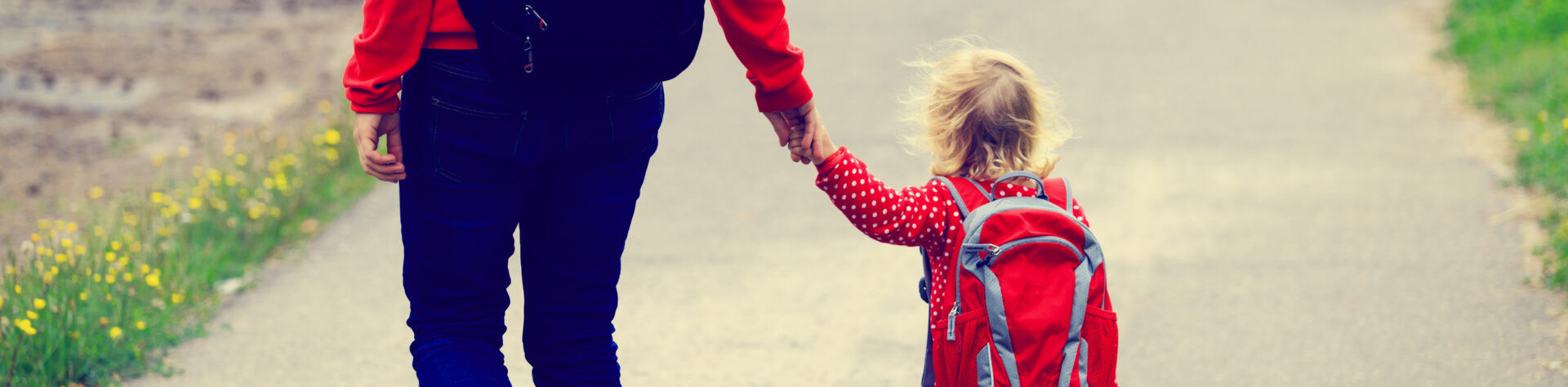 Mother holding hand of little daughter with backpack